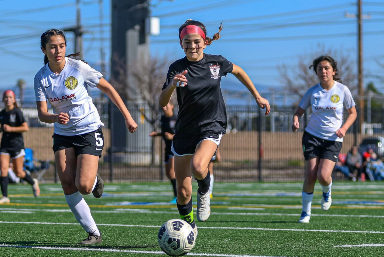 Editorial Strikers girl dribbling in black jersey, black shorts and socks, neon cleats and pink headband